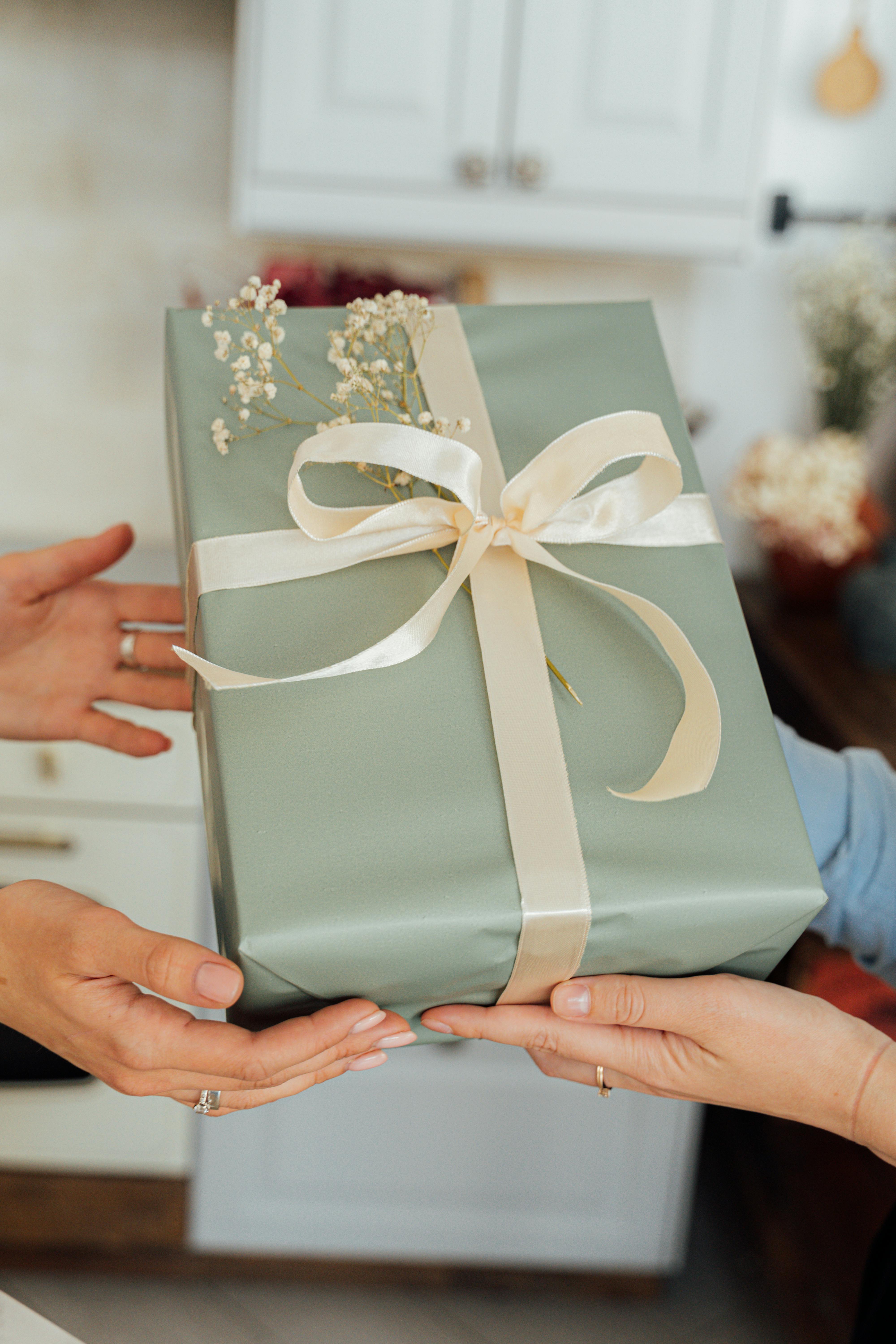 A close-up of two people exchanging a beautifully wrapped gift indoors.